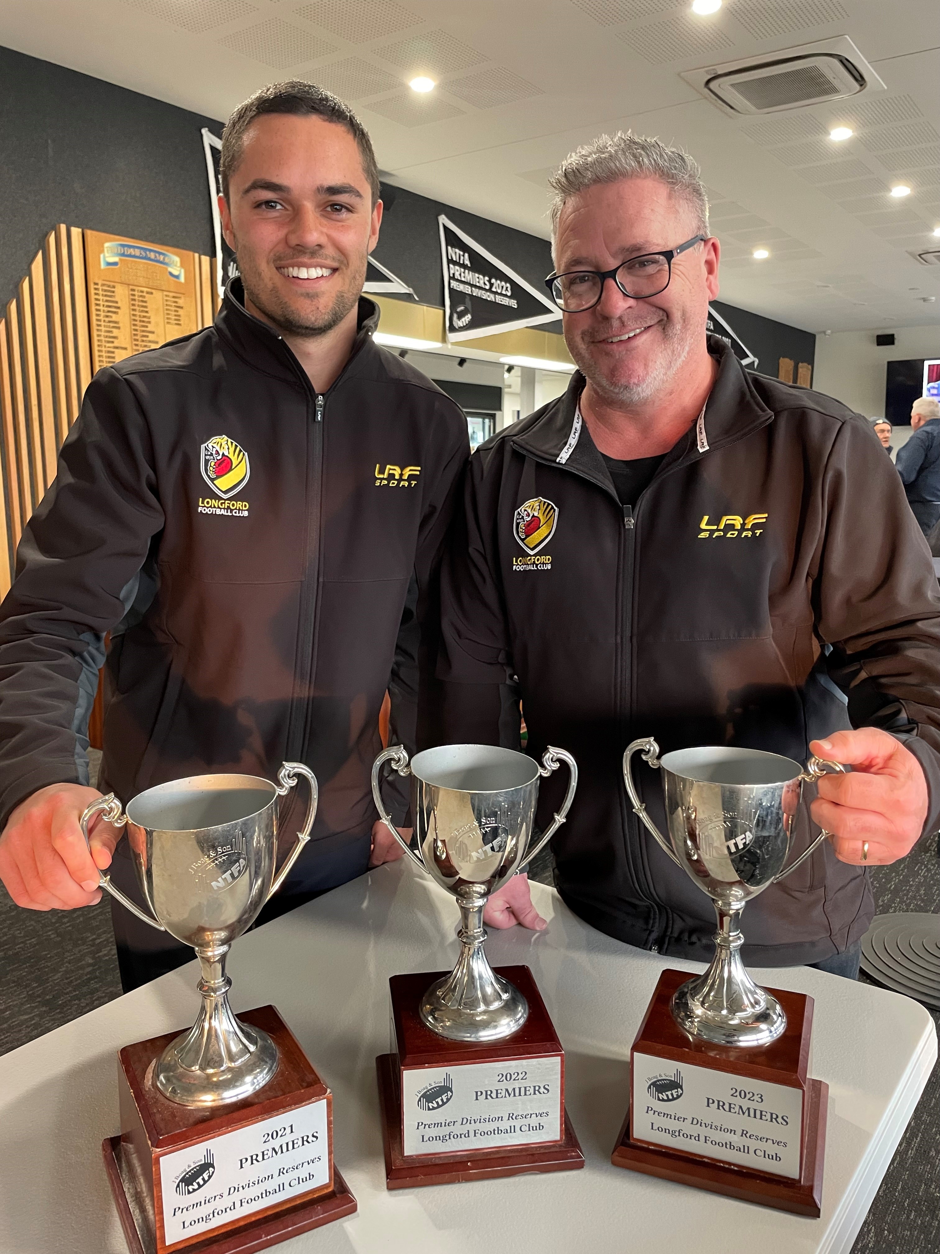 Longford Football Club president Rob Moore and reserves coach Dylan Headland with premiership cups from the past three years.